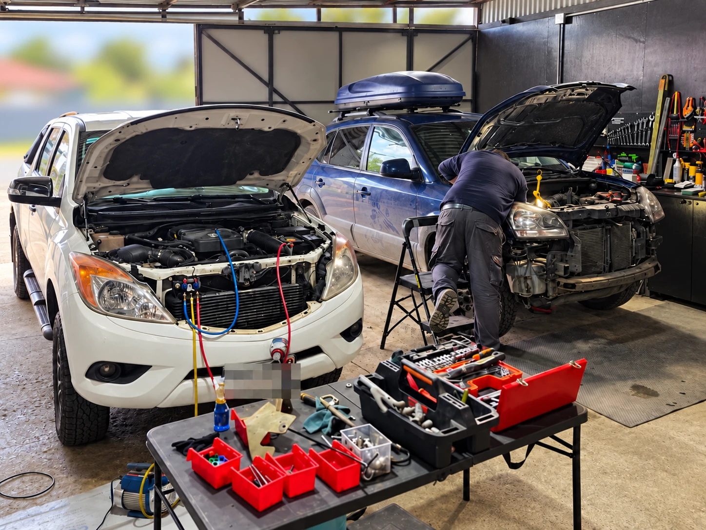 Técnico trabajando en dos vehículos con el capó abierto en el taller de Hualpén