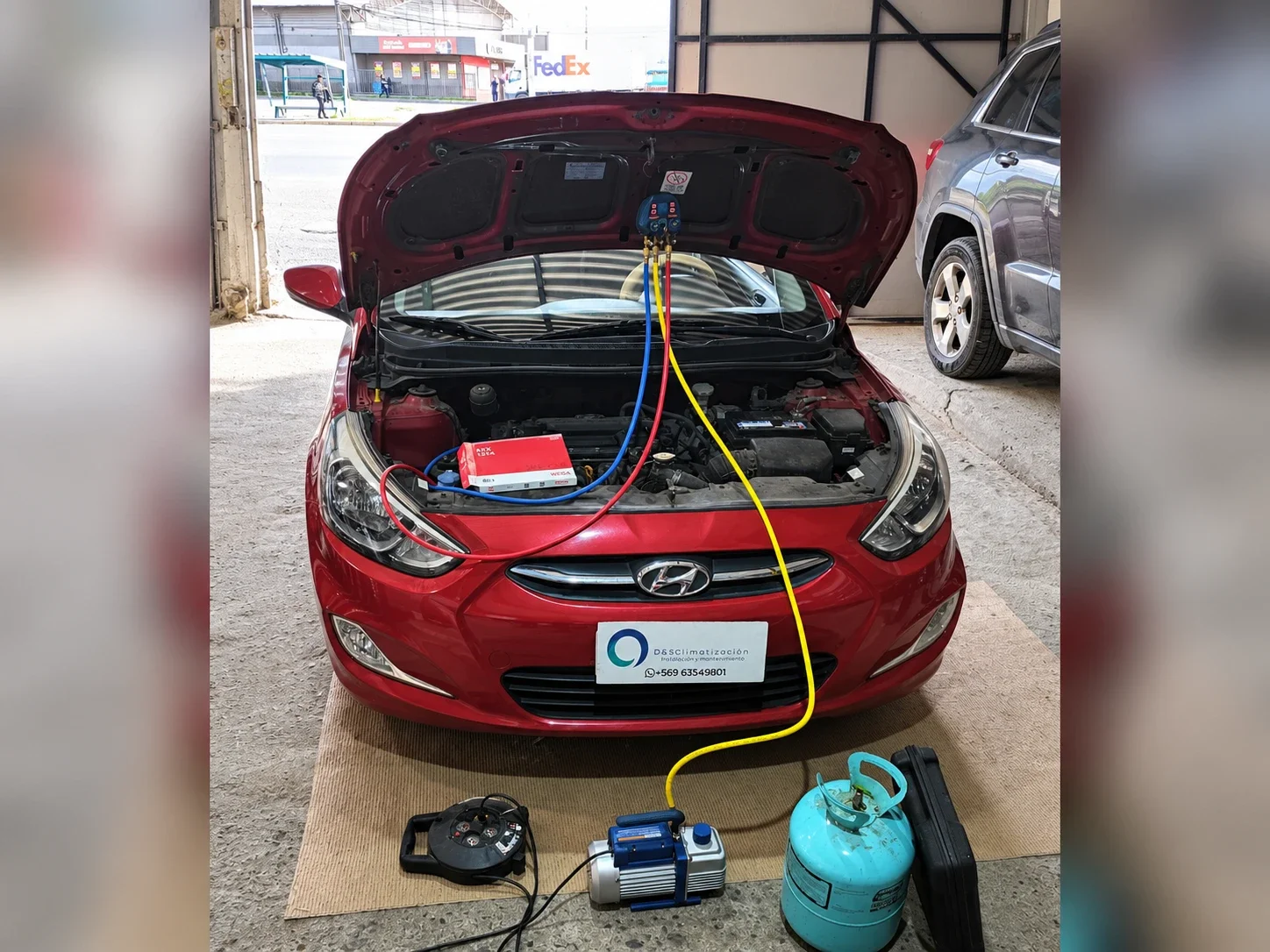 Carga de refrigerante en un auto rojo con manómetros, bomba de vacío y cilindro